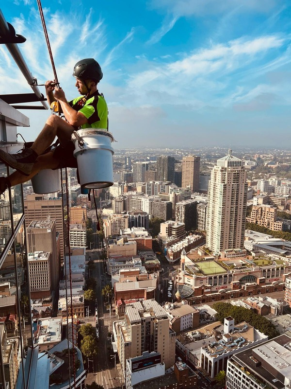 Rope access technician working on a Sydney high-rise façade above the city
